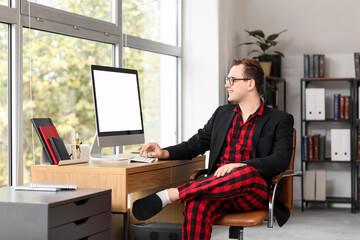 Young businessman working with computer in office. National Wear Your Pajamas to Work Day