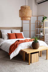 Comfortable bed and bench with houseplant in interior of stylish bedroom