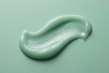 Glossy mint green cosmetic cream smear isolated on matching pastel surface showing smooth texture