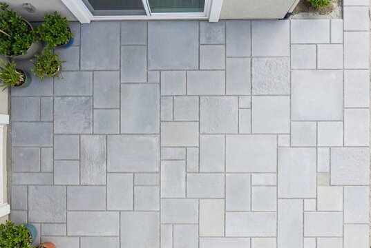Top down view of a light grey concrete paved patio with a patterned stone layout