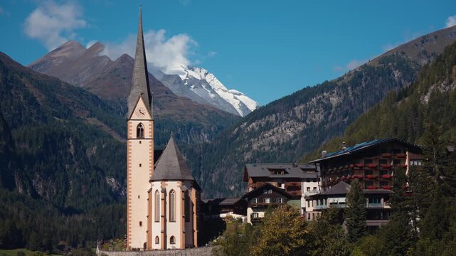 Fixed view of Heiligenblut church and alpine chalets with mountains behind.