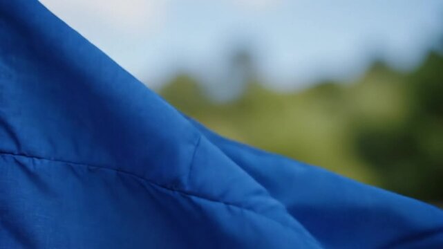 Close-up of Vibrant Blue Fabric Waving in the Wind with Soft Focus Background of Sky and Nature
