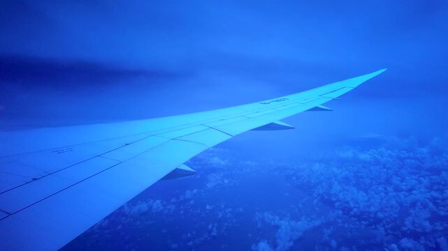 Airplane Wing Over Clouds During Flight With Blue Tinted Window View