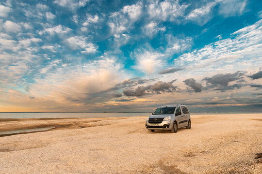 Silver Opel Combo Life parked on a sandy sea beach under blue cloudy sky. Taganrog. Russia. May 20, 2024