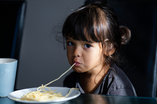 Cute girl slurping noodles in kitchen. Child eating spaghetti with hungry expression. Healthy meal with child. Kid eat spaghetti. Toddler eating pasta lunch indoors. Little child girl tasting pasta.