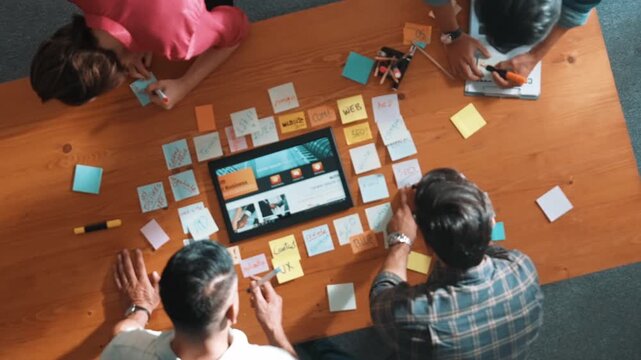 Top view of business people working together to design web design. Aerial view of designer brainstorming and discussing about website interface and looking at tablet with digital design. Symposium.