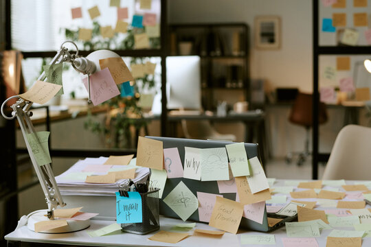 Office desk covered with colorful sticky notes surrounding closed laptop and desk lamp, business workspace showing brainstorming process and creative planning in modern office environment