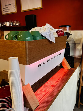 Elektra espresso machine on wooden counter with green cups and towels in a cafe setting
