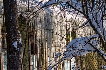 Sparkling jumbo icicles cascade from a weathered wooden home's cornice, illuminated by brilliant sun. A captivating scene of frigid beauty © PhotoChur