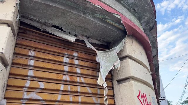 Close-up of peeling paint and weathered facade with metal shutter, stains, and graffiti marks.