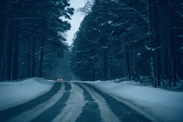 Car driving on a snow covered forest road at dusk, highlighting the journey through cold wilderness and the challenges of winter travel in a remote natural environment