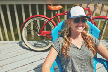 Calm, smile and sunglasses with woman outdoor for shades, summer vacation and weekend break. Happiness, eyewear and peace with female person on deck chair of home for relax, space and holiday trip