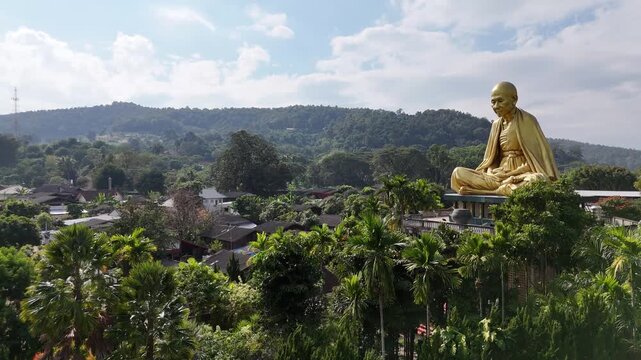 Aerial view of the giant golden statue of Kruba Srivichai, the patron saint of Lanna, surrounded by mountains in Chiang Rai, Thailand.