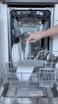 A man opens a dishwasher after a wash cycle and checks the cleanliness of the dishes. kitchen appliance concept