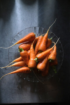 Fresh Organic Baby Carrots in Glass Bowl on Dark Surface, Top View