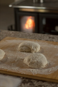 Fresh bread dough balls resting on a floured wooden board with a warm wood stove in the background