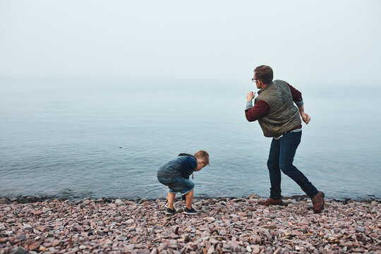 Dad, child and throw rock by river with connection, game and bonding together on weekend break. Space, man and son play outdoor by lake with stone skimming, development and fun for holiday memory.