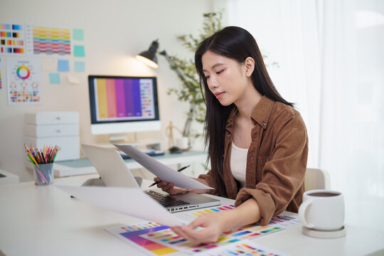 Young graphic designer reviewing color palette samples while working on a laptop in a modern home office.
