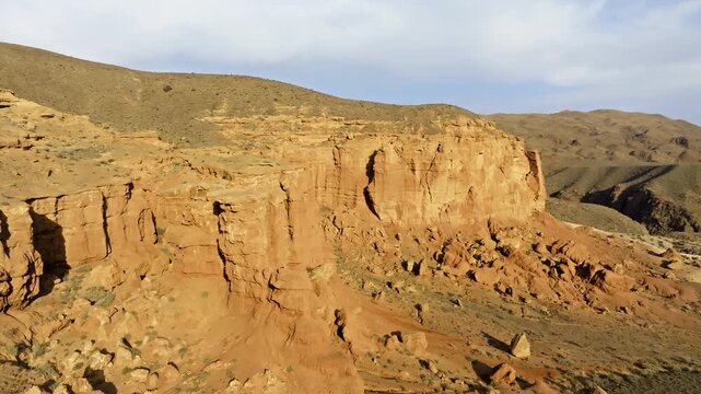 Eroded sandstone rock formations in barren landscape of Kyrgyzstan, forward moving drone view at evening sun light.