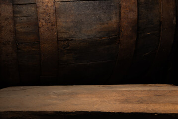 Moody oak cellar with wood table, dim amber light, aged barrel backdrop, rough plank surface, strong grain texture, warm brown