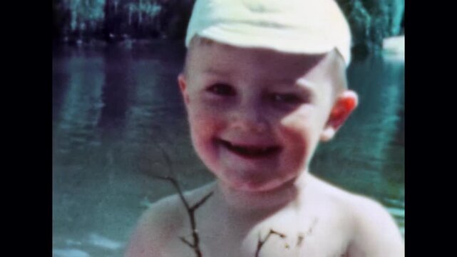 Close up, adorable baby boy portrait on blue water backdrop enjoying summer vacation. Healthy happy child smiles, laughs looking at camera at family holiday. Old film. Archival retro. Vintage archive