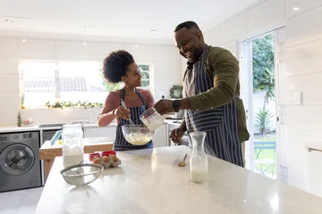 Fotobehang Koken African American couple preparing batter on kitchen island in striped aprons using glass bowl, jug  © wavebreak3