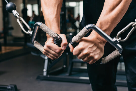 Strong male hands holding cable machine handles during workout in a gym.