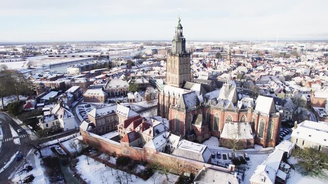 Sunlight illuminating medieval Hanseatic Dutch tower town Zutphen in the Netherlands covered in snow with historic heritage buildings and river IJssel passing by in the background behind Walburgiskerk