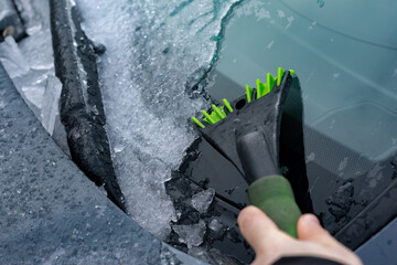 Close-up of hand scraping ice off a car windshield with a green ice scraper on a cold winter day, highlighting safety and seasonal change.