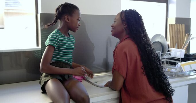 African adult woman and youth girl passing soap, causing washing hands, laughing at kitchen sink