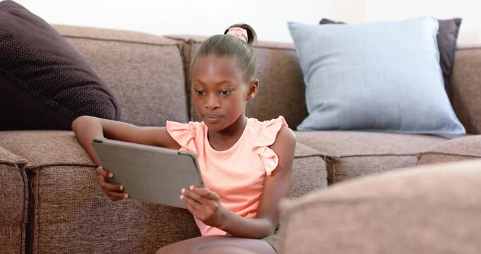 Preteen female wearing pink ruffle top, scrunchie sitting at home using tablet, angling for viewing