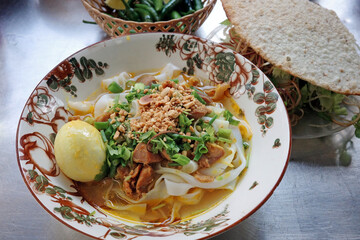 close up of a traditional bowl of mi quang chicken noodles with yellow turmeric rice noodles peanuts herbs and rice cracker a famous local street food in danang vietnam