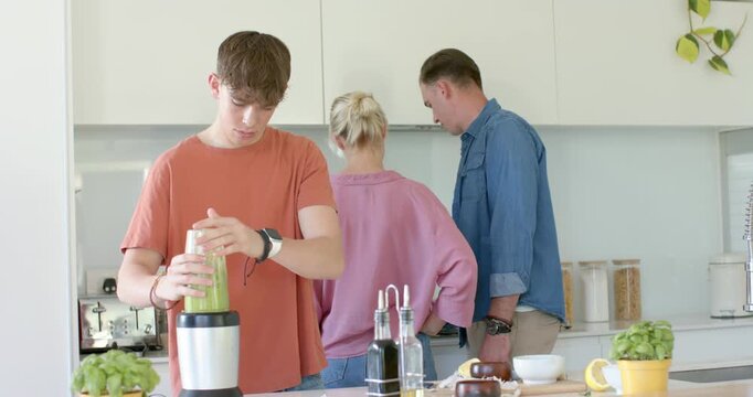 Family teenage son placing blender cup on base, securing lid, preparing green smoothie at island