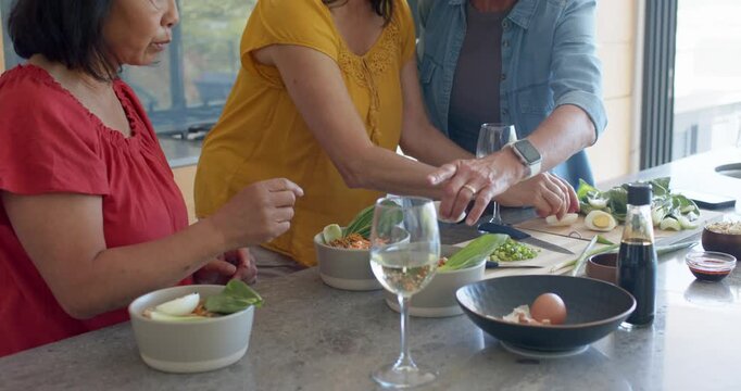 Diverse female friends assembling bowls at kitchen island, right woman using knife halving egg
