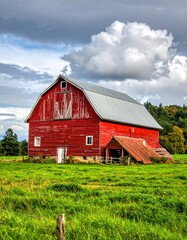 Obraz premium Rustic Red Barn Amidst Green Pasture Under a Cloudy Sky A Charming Rural Scene.