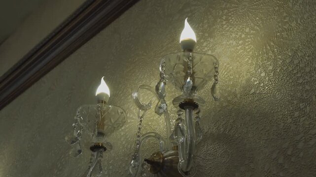 View of a crystal chandelier sconce attached to a wall with light bulbs in the form of candles.