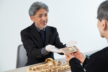 スーツ姿に白手袋の中年男性がサックスを丁寧に検査・査定しているシーン © ponta1414