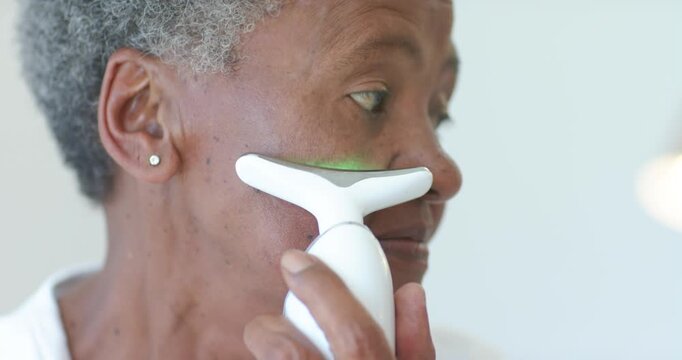 Senior African American woman using T device skin touch lighting LED gliding under eye for skincare