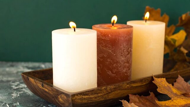 Three lit candles in a wooden tray with autumn leaves, creating a warm and inviting atmosphere.