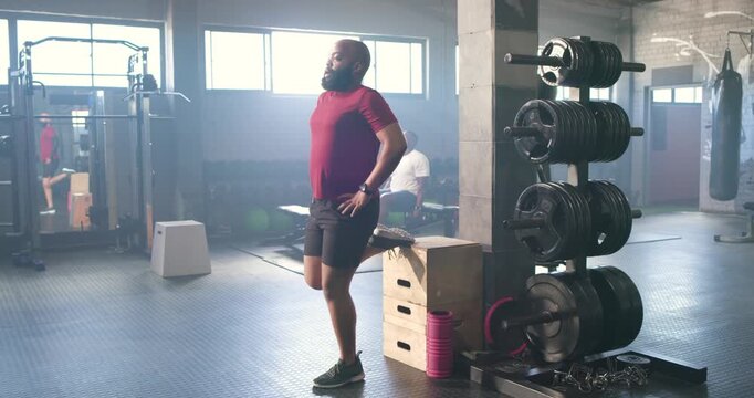 African American man starting with foot on plyo box, performing hamstring stretch in gym warming up