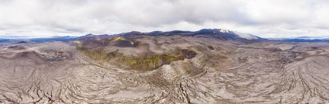 Aerial view of a stark, cracked landscape with patches of vibrant green moss, mountains and craters on northern slope of Hekla volcano, in 360 degrees panorama, Hekla, Sudurland, Iceland.