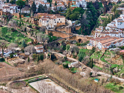 Aerial view of ancient bridges arching over lush greenery, connecting historic buildings in a timeless landscape, Ronda, Andalusia, Spain.