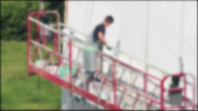 Defocused Man In Overalls Renovates Building Exterior With White Paint.