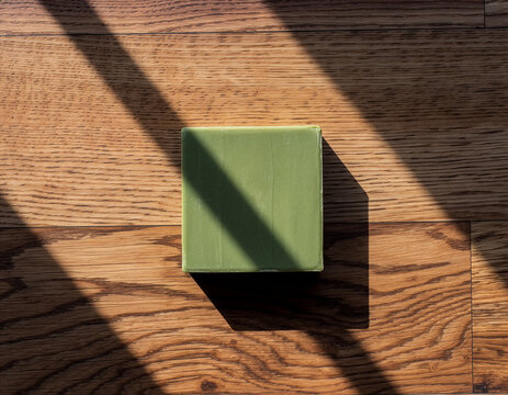 Green natural soap bar on wooden surface with dramatic sunlight shadows