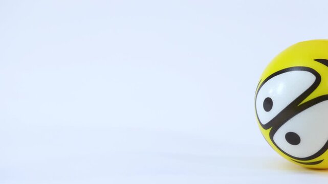 Yellow Emoji Stress Ball Rolling Across a Plain White Surface