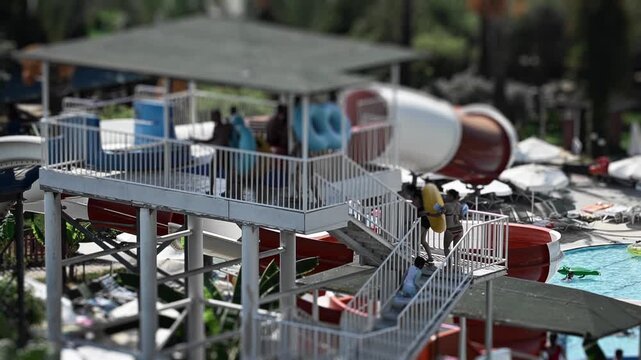 Aquapark. Fun recreation attraction with inflatable rings for thrilling descent into pool. People ascend stairs, carrying inflatable rings. Multiple colorful slides await thrilling descent. Sunny day.
