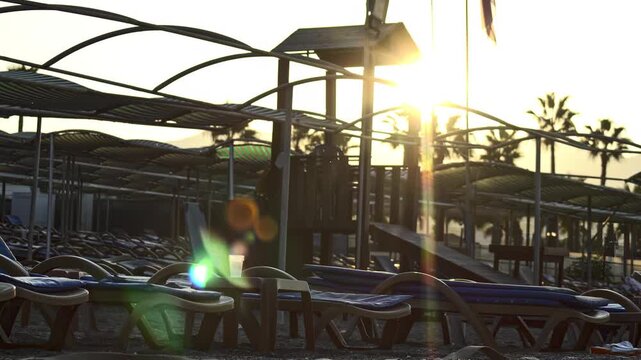 Tranquil beach resort morning, rows of unoccupied sunbeds and beach umbrellas. Vacation in Turkey, rest. Warm light of rising sun creates dramatic lens flare. Golden hour light illuminates peaceful se
