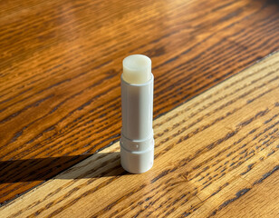 White lip balm tube mockup on wooden surface with sunlight shadows