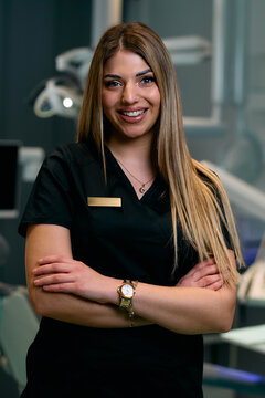 Confident Female Healthcare Professional In Black Scrubs Smiles With Crossed Arms In Clinical Setting Today