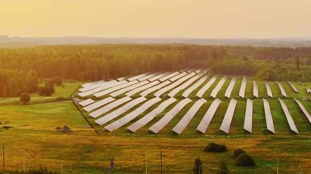 Drone slides sideways over solar panels by forest glowing in sunrise light